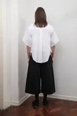 Bermuda negra unisex de corte sastrero, con pretina elástica, tiro bajo, bolsillos laterales y cierre lateral. Presenta un pliegue delantero de gran tamaño.