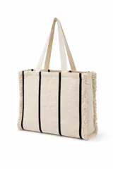Bolso tote bag tejido a mano en color beige con rayas verticales negras y bordes deshilachados. Tiene dos asas de mano.