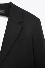 Blazer negro de cuello solapa y manga larga con hombreras. Tiene bolsillos de vivo en delantero y pecho, detalle de aberturas en espalda, botón y forro interior a tono.