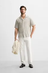 Camisa de hombre relaxed fit confeccionada en tejido de algodón a rayas verticales blancas y negras. Tiene cuello bowling, manga corta, bajo con aberturas laterales y cierre frontal de botonadura.