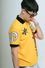 Chomba amarilla de piqué con cuello y puños negros, corte regular, bordado y aplique premium.