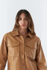 Sobrecamisa color marrón de poliuretano, con cuello clásico, cierre frontal con botones a presión, mangas largas con puños abotonados, dos bolsillos tipo parche con solapa y botón en el pecho.