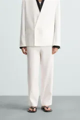 Pantalón blanco de lino con corte relajado (relaxed fit), cintura elástica, bolsillos frontales y un bolsillo trasero de vivo.