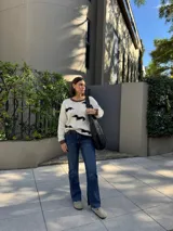 Sweater tejido color crema con cuello y puños acanalados en color naranja. Presenta un diseño bordado de un perro salchicha negro con un moño naranja.