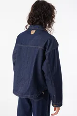 Camisa corta de jean azul con terminación redondeada en el ruedo. Presenta dos bolsillos plaqué bordados con motivo de montaña y detalle de pespunte a contratono.