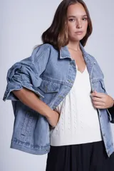 Campera clásica de jean celeste con cuello camisero, bolsillos frontales con solapa y cierre con botones metálicos. Presenta detalles de pequeños brillos blancos dispersos en la parte delantera y las mangas.