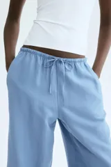 Pantalón de corte recto y holgado en tejido de mezcla de lino color celeste. Cuenta con cintura elástica con cordón de ajuste, bolsillos laterales y bolsillos traseros insertados.