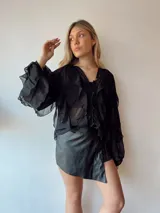 Blusa negra traslúcida con volados y mangas largas abullonadas.