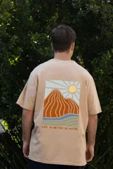 Remera color beige de manga corta con cuello redondo y estampado de un sol con montañas en el pecho.
