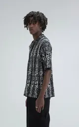 Camisa de manga corta tejida de punto abierto (símil crochet), calce oversize, color negro con diseño abstracto en beige.