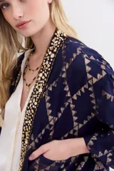Kimono corto azul marino con estampado geométrico dorado, confeccionado en viscosa jacquard con lurex. Presenta guarda bordada en piedras y canutillos, y forrería interior.