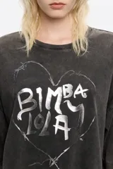 Camiseta de algodón negra con efecto gastado, corte oversize y mangas cortas anchas. Presenta un estampado frontal de un corazón dibujado con alambre de púas, conteniendo el texto "BIMBA LOLA" en su interior.