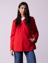 Campera impermeable roja con cierre central, bolsillos delanteros y lazo de ajuste en la cintura. Tiene avíos metálicos plateados y cierre oculto en la espalda para autoguardado.