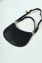 Cartera de hombro negra con forma de media luna, confeccionada en material con textura de pelo o cuero. Presenta costura decorativa gruesa en el borde y correa ajustable con herrajes metálicos plateados.