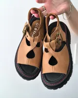 Sandalias de cuero color marrón claro, con suela de goma negra y pespuntes rojos.