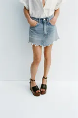 Minifalda de denim azul con tiro medio, trabillas, cinco bolsillos, roturas y bajo desflecado.