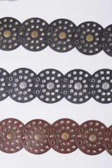 Cinturón de cuero con diseño de discos circulares superpuestos, adornados con tachas y hebillas redondas grabadas. Disponible en negro, marrón y con hebillas en tonos dorado y plateado.