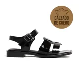 Sandalias bajas de cuero charol negro, con tiras anchas cruzadas en el empeine y hebilla lateral ajustable.