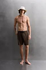 Bañador corto color marrón con cintura elástica negra ajustable con cordón. Tiene un bolsillo lateral con cierre de cremallera y costuras planas termofijadas.