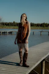 Vestido corto marrón de gamuza sintética, sin mangas, con escote en V y detalle de flecos en el ruedo. Presenta apliques bordados en el frente y laterales.