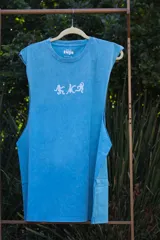 Musculosa sin mangas, color celeste con efecto acid wash, cuello redondo y amplias sisas. Estampado frontal en blanco con figuras abstractas y texto.