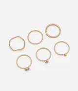 Set de seis anillos dorados con diferentes diseños: tres anillos finos con strass de colores, un anillo martillado, un anillo con textura trenzada y un anillo liso tipo alianza.