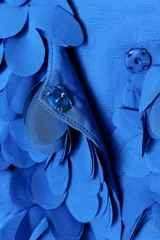 Chaqueta azul con cuello redondo y manga larga, con apliques de pétalos en toda la prenda y cierre frontal con botón a presión oculto.