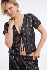 Top negro con estampado de moños blancos, escote en V y mangas cortas.