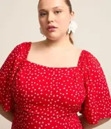 Vestido midi rojo con estampado de lunares blancos, escote cuadrado, mangas cortas con volados y falda acampanada. Presenta detalle de lastex en la espalda y abertura frontal. Confeccionado en viscosa.