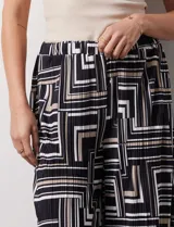 Pantalón ancho estilo palazzo, de seda fría plisada con estampado geométrico en negro, blanco y beige. Tiene pretina ancha elastizada y largo crop.