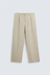 Pantalón de corte holgado (wide fit) en color beige, confeccionado en tejido con mezcla de lyocell. Presenta pliegues frontales en la cintura, bolsillos laterales y bolsillos traseros de doble vivo. Cuenta con cierre frontal de cremallera y botón.