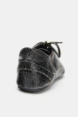 Zapato plano de cuero negro con efecto desgastado y cordones.