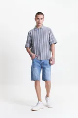 Camisa oversize de manga corta con cuello clásico y cierre abotonado. Diseño a rayas verticales en tonos gris y blanco. Confeccionada en algodón.