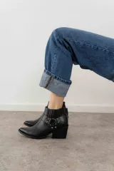 Bota corta de cuero negro con puntera fina, taco cuadrado y correa con hebilla metálica.