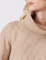 Buzo de punto grueso color beige, con cuello volcado y textura en relieve. Tiene mangas largas de corte hombro caído y puños anchos.