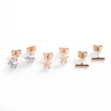 Set de tres pares de aros mini color oro rosa en acero quirúrgico: un par con forma de cubo con cristal, un par con forma circular y un par con forma de barra horizontal.