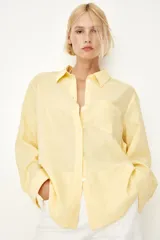 Camisa amarilla de tejido liviano de mezcla de lino y viscosa con cuello, botones adelante y canesú de doble capa con pliegue de caja en la espalda. Modelo de manga larga con bolsillo superior abierto, puños abotonados y bajo redondeado.
