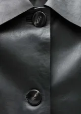 Chaqueta corta de cuero ovino color negro, con cuello camisero, cierre frontal con botones y dos bolsillos de solapa.