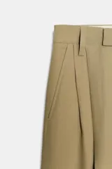 Pantalón ancho de tiro medio, color verde oliva, confeccionado en lino 100%. Presenta pliegues marcados en la parte delantera y bolsillos laterales ocultos.