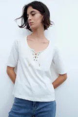 Remera blanca de manga corta con escote redondo y cordones cruzados con ojalillos metálicos.