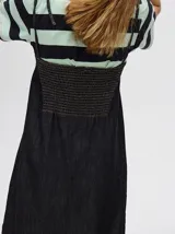 Vestido midi de denim algodón color marrón, con escote recto y tirantes finos ajustables con lazos. El corte es suelto y termina con un ruedo con semi-volado.