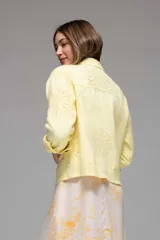 Campera corta color coral con cuello camisero, cierre frontal con botones, bolsillos de parche en el pecho y mangas largas con puños abotonados. Presenta calados tipo broderie en hombros, mangas y espalda.