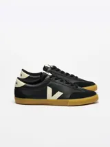 Zapatillas Veja modelo Volley, color negro con logo lateral en blanco y suela de goma color caramelo.