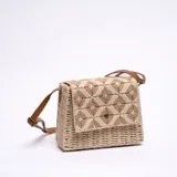 Bandolera de paja color beige con diseño geométrico en tonos marrones y correa de cuero sintético marrón.