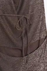 Vestido largo de fiesta confeccionado con hilo metalizado color marrón. Tiene cuello halter con lazada, escote drapeado, espalda descubierta con tira ajustable y cierre lateral con cremallera oculta.