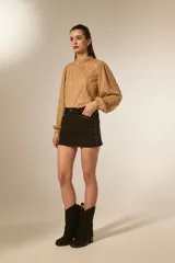 Minifalda marrón de gamuza sintética con tiro alto y detalles de tachas doradas a lo largo de los costados y bolsillos delanteros.