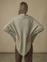 Poncho de tejido lurex color verde oliva con brillo sutil, de corte amplio y manga larga con puños acanalados. Presenta un bajo asimétrico con caída diagonal.