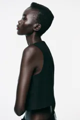 Chaleco corto negro con cuello redondo, sin mangas y cierre frontal con botones dorados.