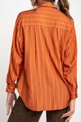Camisa oversize color ladrillo con rayas verticales blancas y rosadas, de mangas largas y botones de madera.