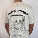 Remera color crudo de corte clásico con estampa en la espalda de una ventana con vista a la playa y la frase "Easy Mornings" y "Pause & Coffee".